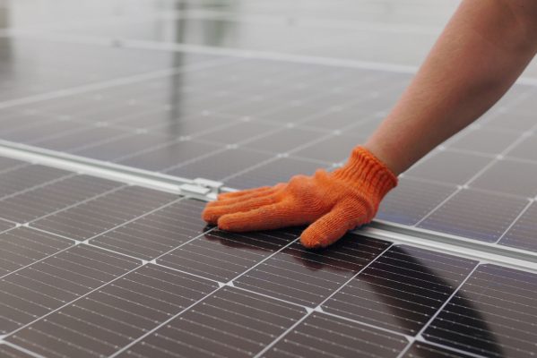 Hand mit Arbeitshandschuh berührt ein Solarpanel